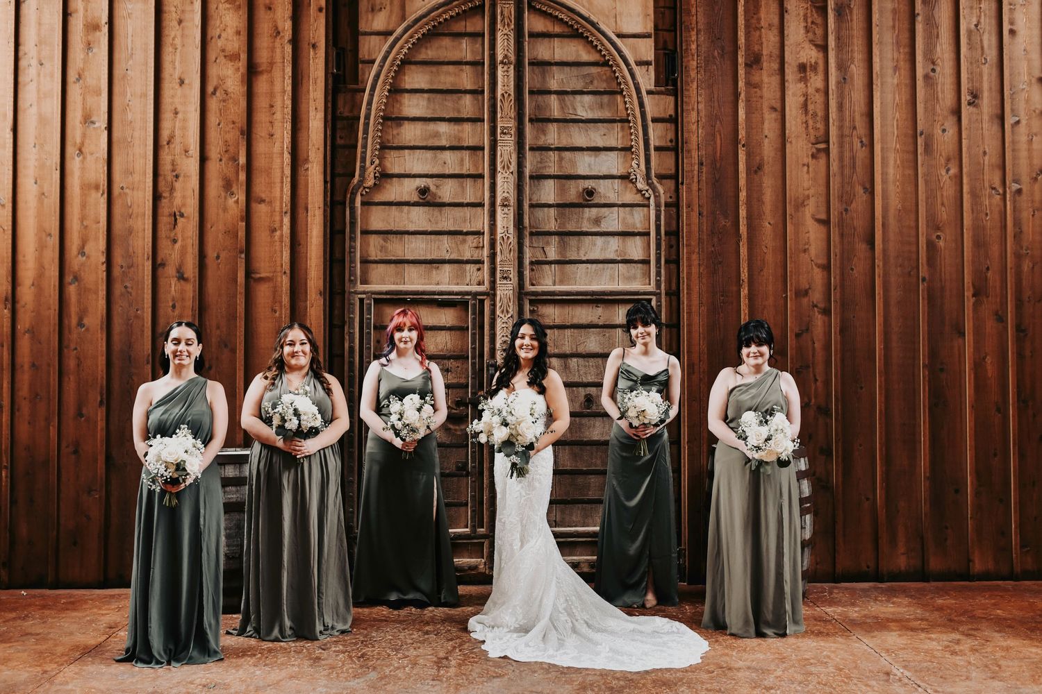 Editorial bridal party portrait featuring mismatched green dresses and organic ivory floral bouquets.