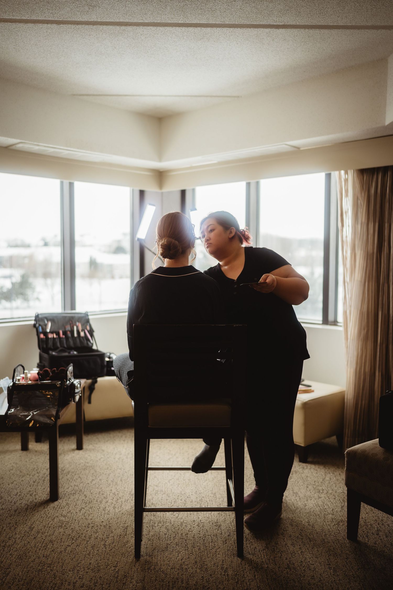 Two people sit together in a bright room with large windows and carpeted floors, creating a contemplative scene.