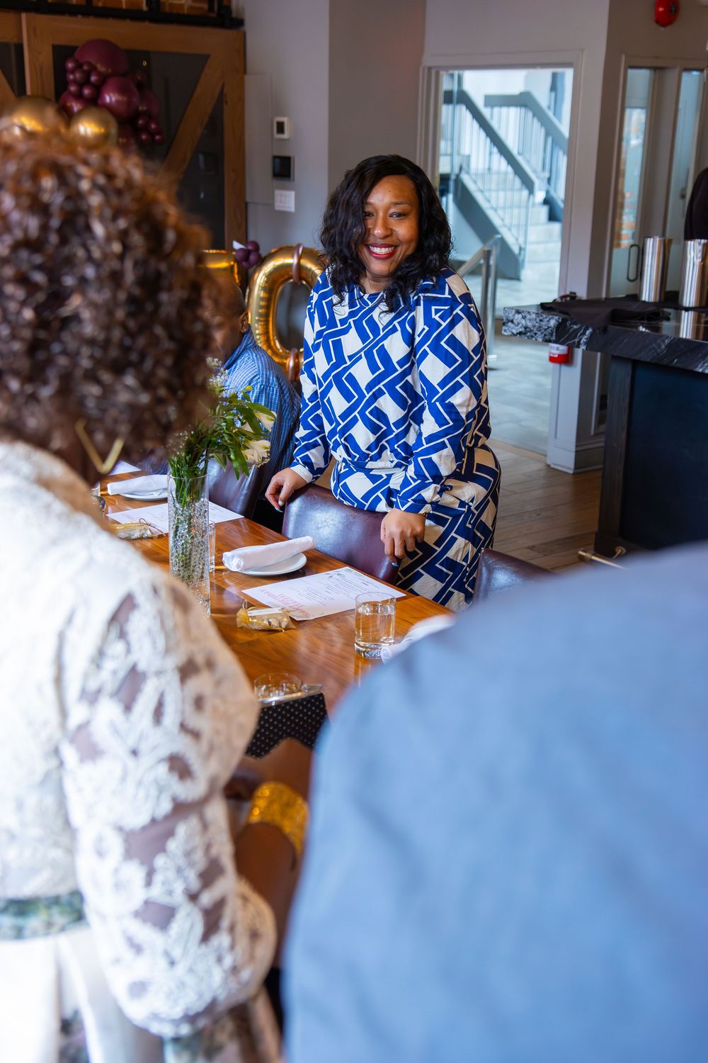 A person wearing a blue and white patterned top sits at a dining table in a modern interior setting.