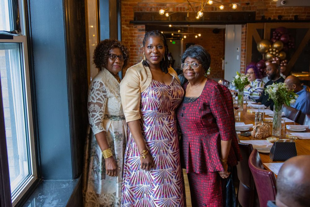 A group of wedding guests in burgundy and pink dresses smile and celebrate at an indoor reception venue.