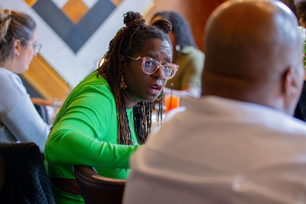 Person in bright green sweater and glasses engaged in conversation at restaurant table.