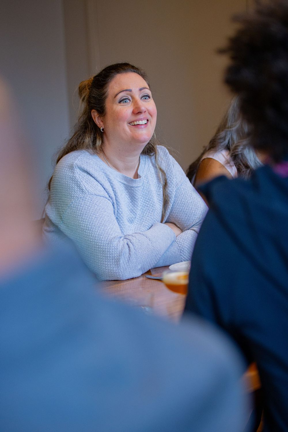 A person wearing a white sweater smiles and laughs during an indoor social gathering.