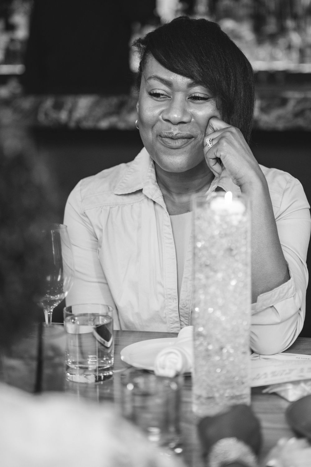 Black and white portrait of woman smiling while sitting at bar with drinks.