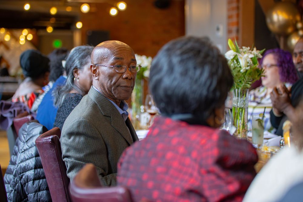 People gather at an indoor event with warm lighting and decorative table settings for a special occasion.