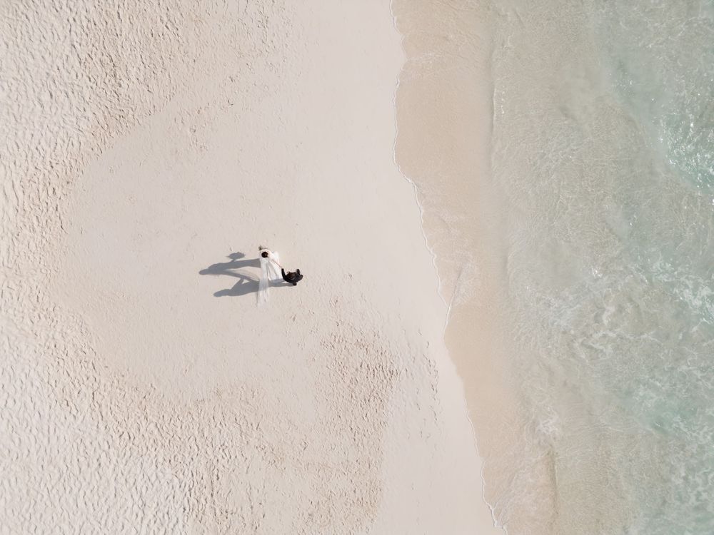 Aerial drone view of couple walking hand in hand on Cancun beach, romantic elopement photography in Riviera Maya.