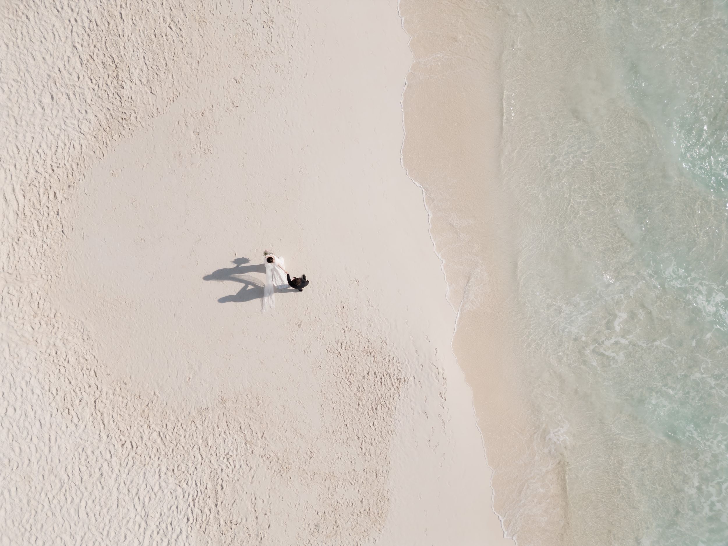 Aerial drone view of couple walking hand in hand on Cancun beach, romantic elopement photography in Riviera Maya.