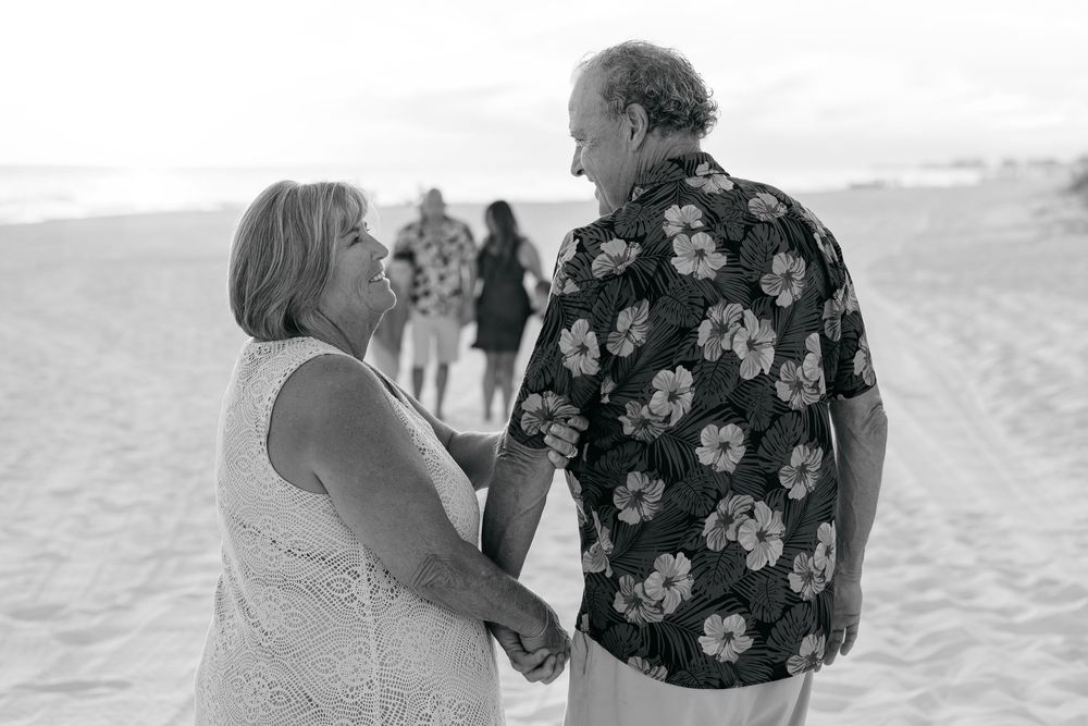 Two people walk hand in hand along a beach shoreline during sunset, creating silhouettes against the sky.