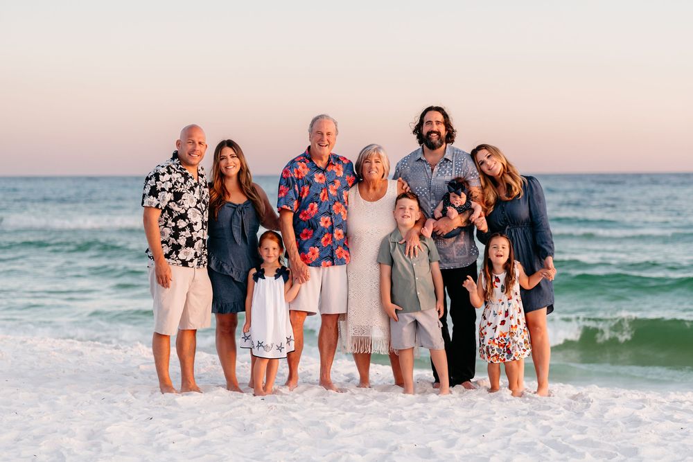 A group poses together on the beach at sunset wearing coordinated casual beachwear in neutral colors.