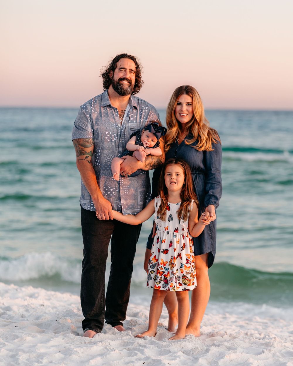 A family enjoys a sunset photoshoot together at the beach with waves crashing in the background.