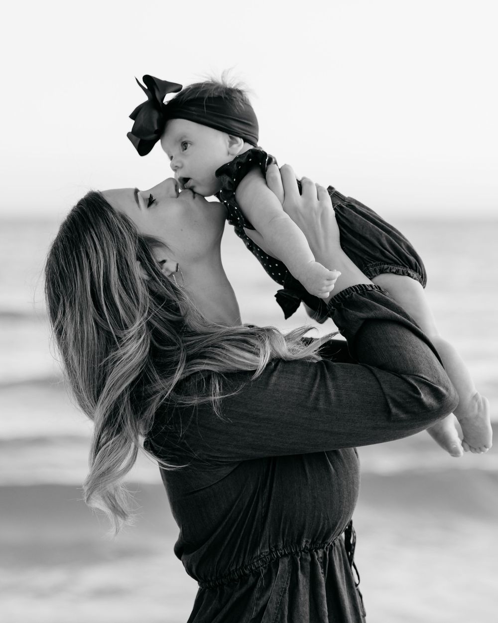 A sequence of black and white photos showing a person in dark clothing holding and lifting a small dog at the beach.
