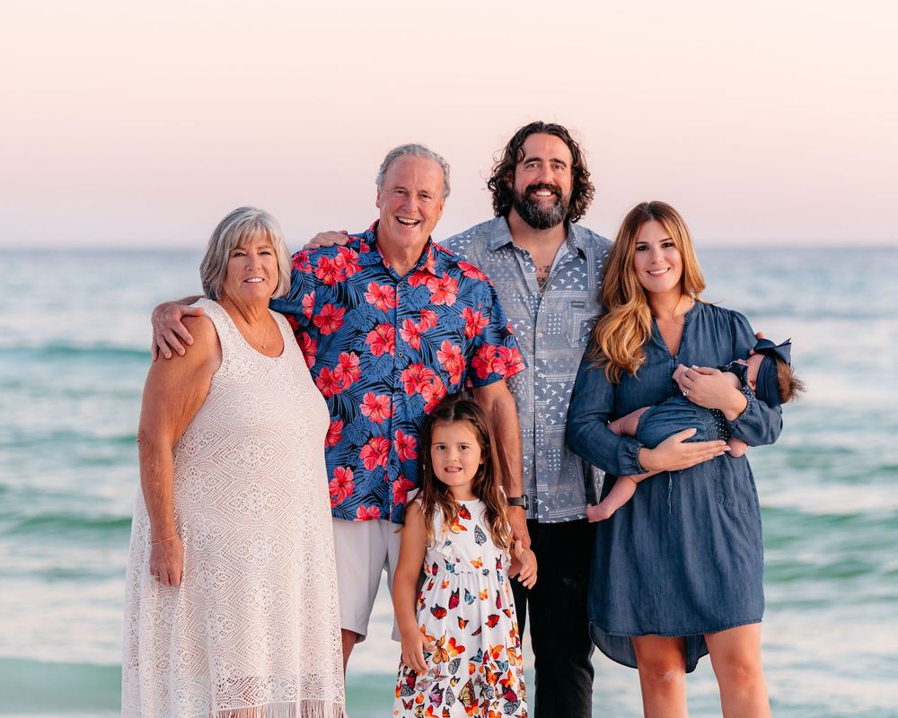 A family group poses together for portraits on the beach at sunset wearing coordinated blue and floral outfits.