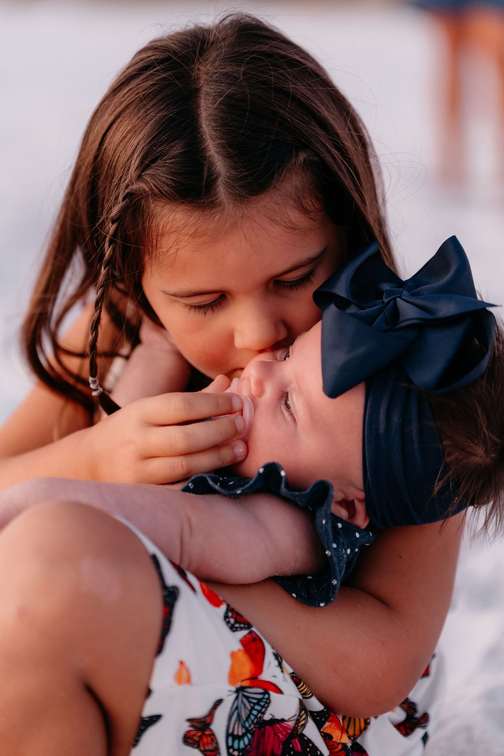 A tender moment between two young children sharing an affectionate kiss in warm sunlight.