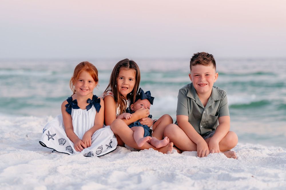 Family members lying together on white sandy beach wearing coordinated blue and white outfits at sunset.