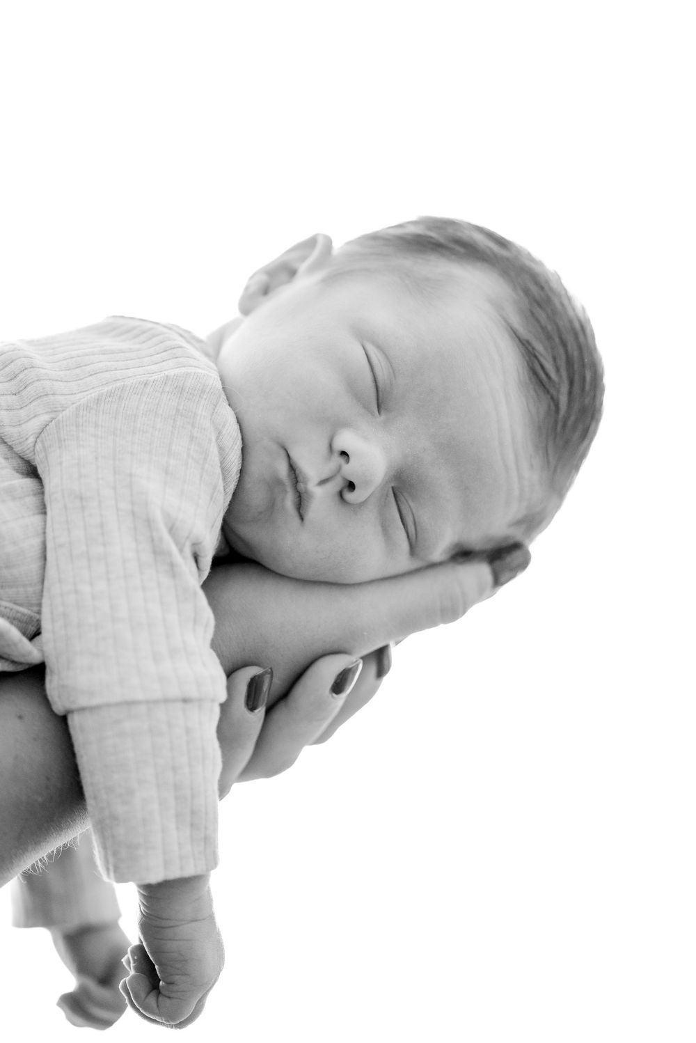 Black and white newborn baby sleeping peacefully in parent's hands against white background.