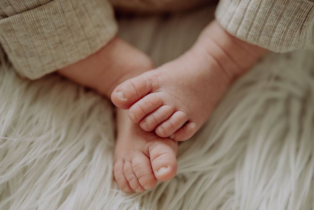 Close-up of tiny newborn baby feet resting on a soft white fluffy blanket.