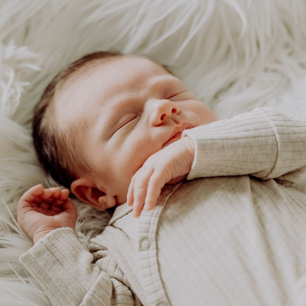 Peaceful newborn baby sleeping on a white fluffy blanket wearing a neutral knit onesie.