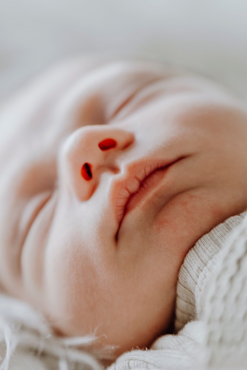 Extreme close-up of a sleeping newborn baby's face wrapped in a soft white knit blanket.