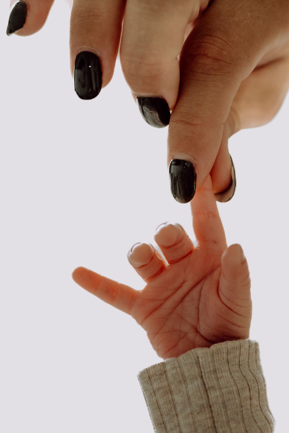 Adult hand with dark nail polish gently touching a newborn baby's tiny outstretched finger.