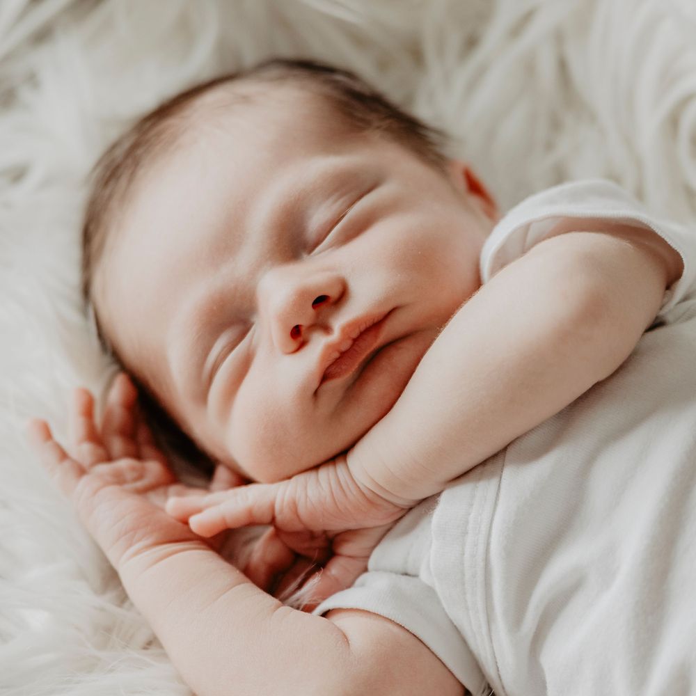 Sleeping newborn baby smiling softly while resting on a white fluffy blanket in parent's hand.