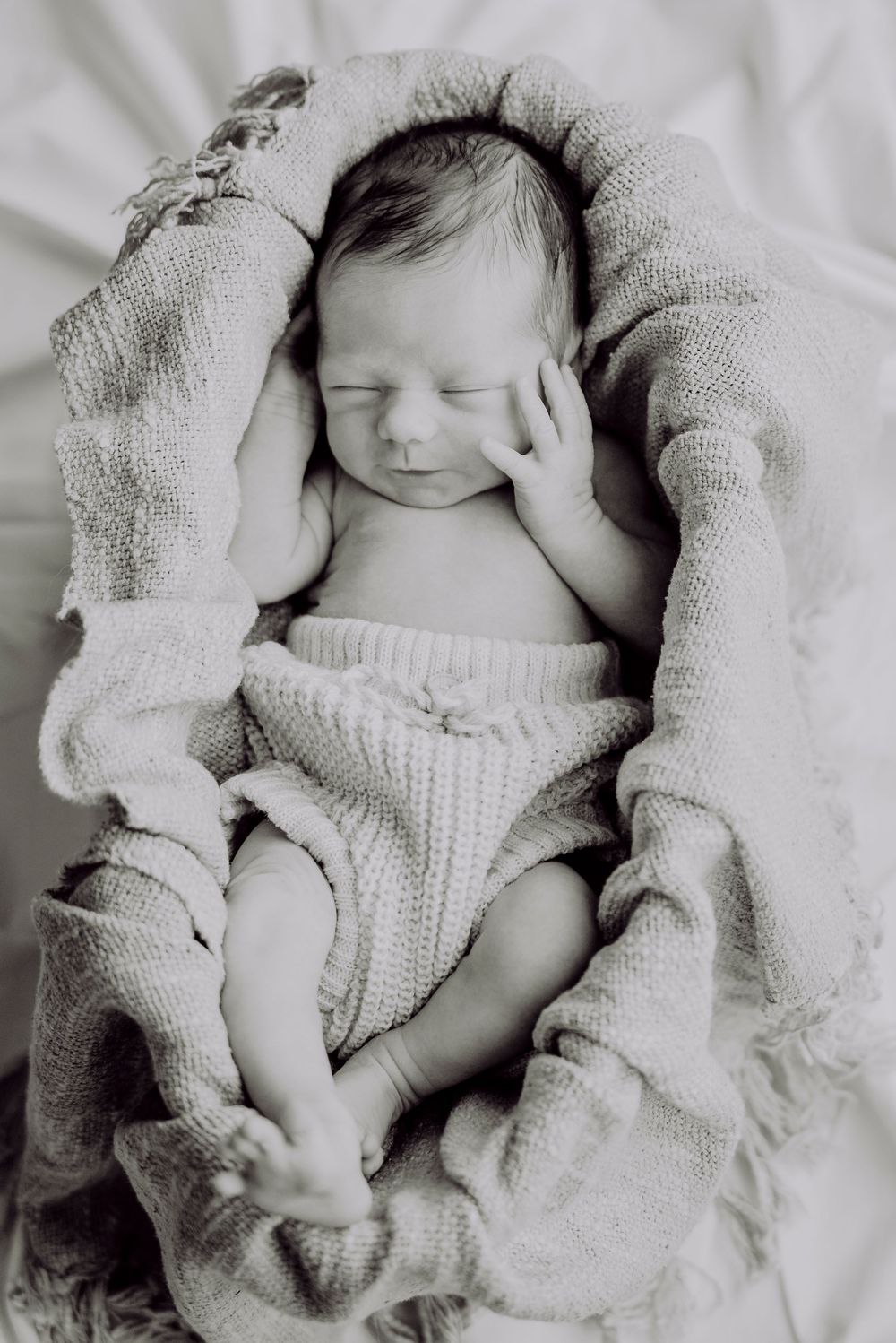 Peaceful newborn baby sleeping wrapped in soft knit blanket, black and white photography.