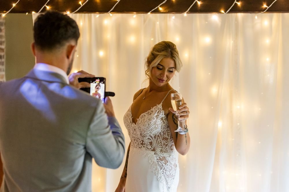 A bride in an elegant lace gown stands before a romantic fairy light backdrop.