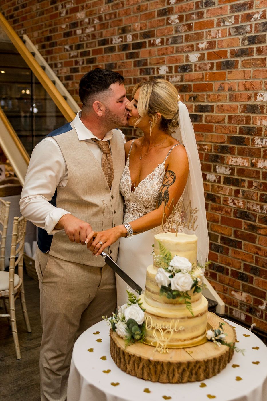 Traditional wedding cake cutting ceremony with white floral decorations on wooden stand.