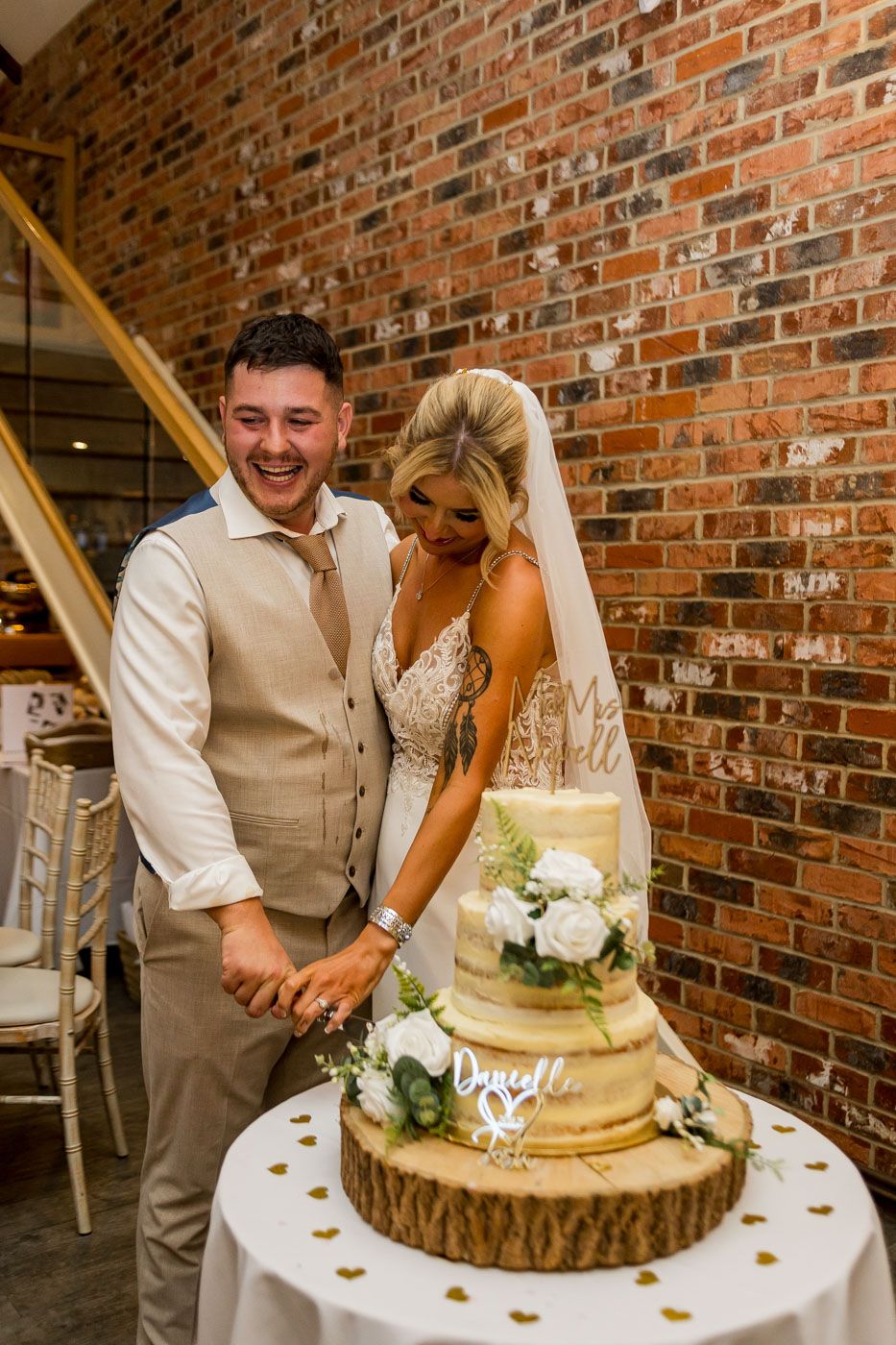 Wedding couple cuts their elegant two-tier cake displayed on a wooden slice at their reception.
