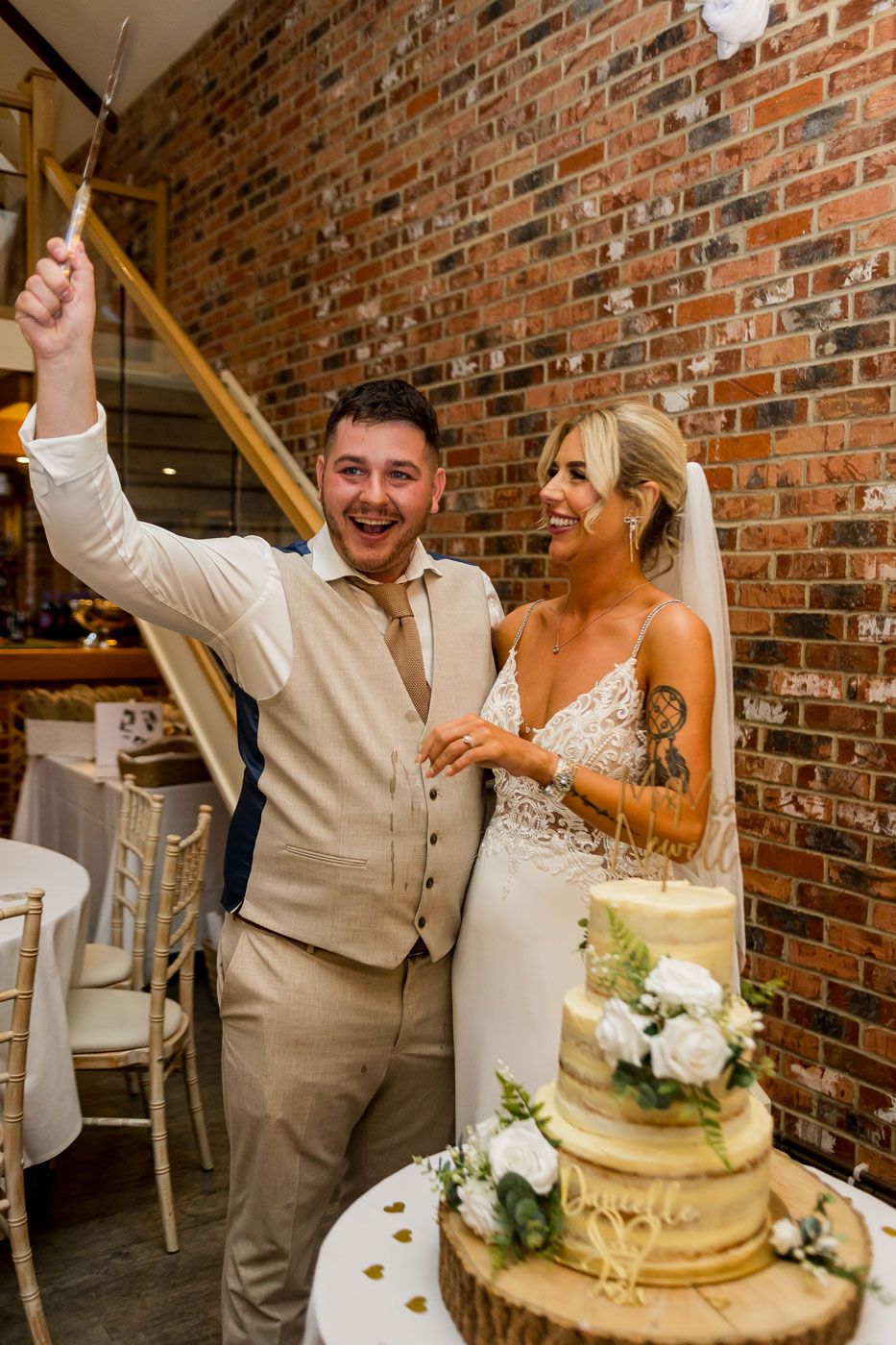 Joyful cake cutting moment at wedding reception with rustic brick wall background.