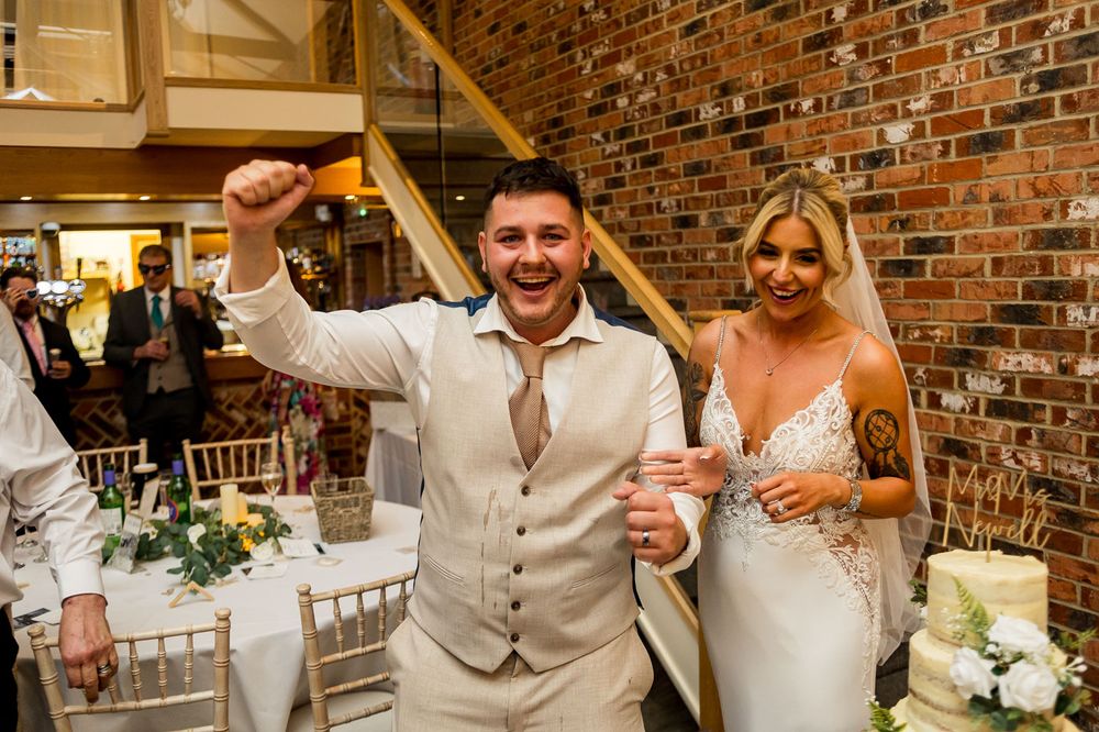 Newlyweds celebrate at their reception in front of a rustic brick wall backdrop.