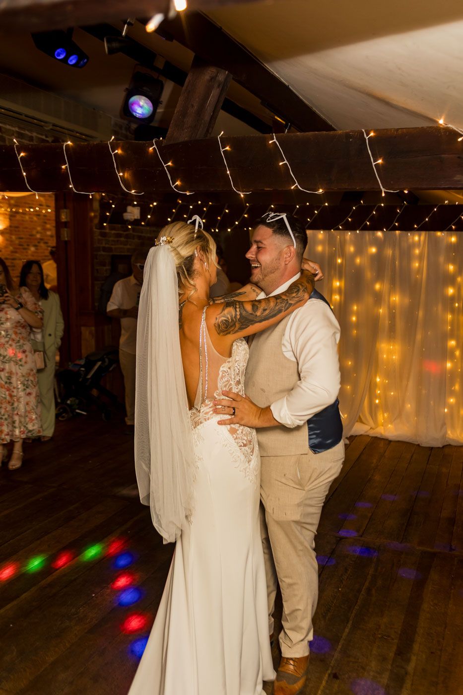 A couple shares their first dance at a rustic wedding reception under twinkling lights and exposed beams.