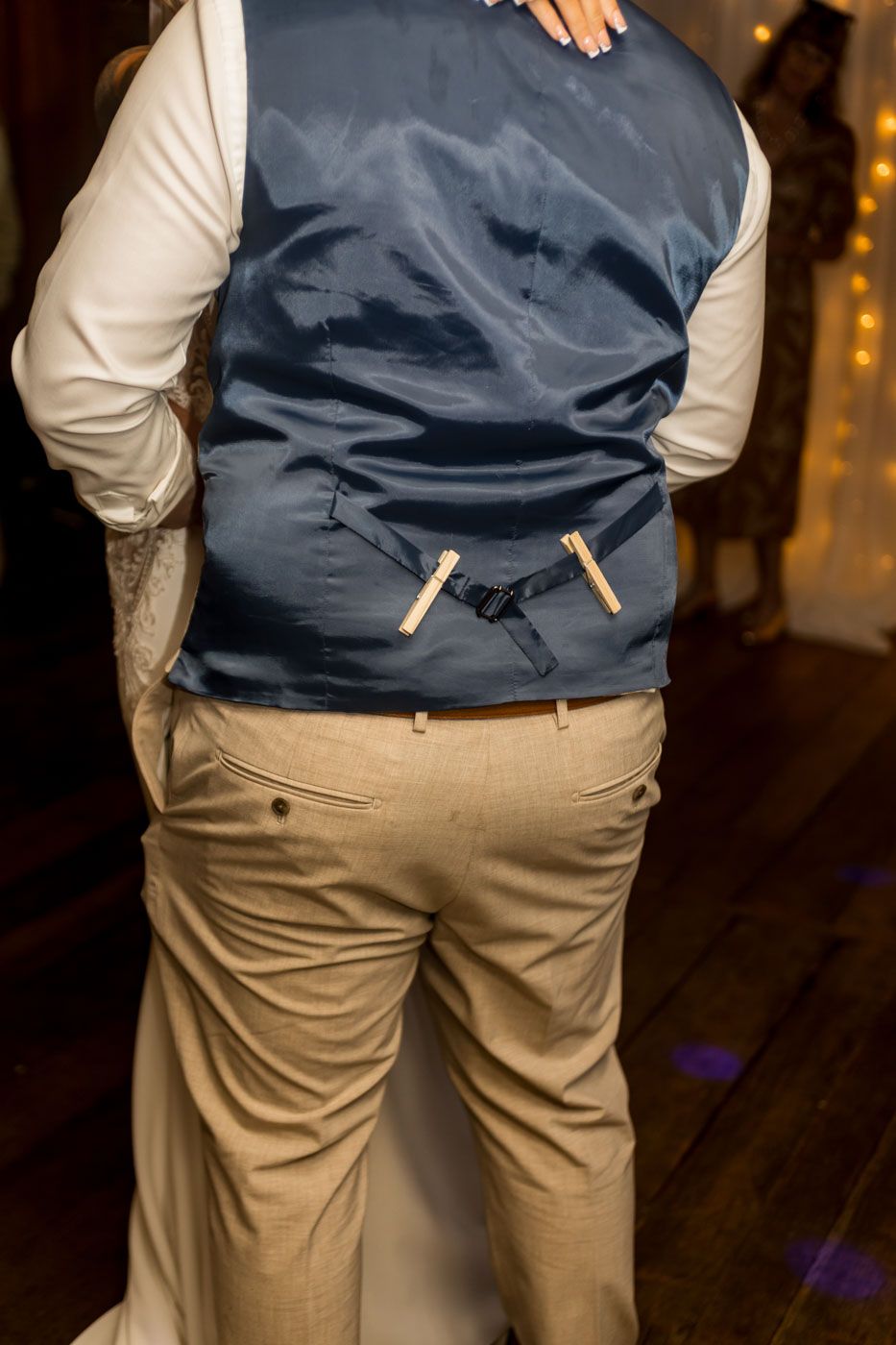 Back view of a groom in tan pants and navy vest showing wedding day attire details.