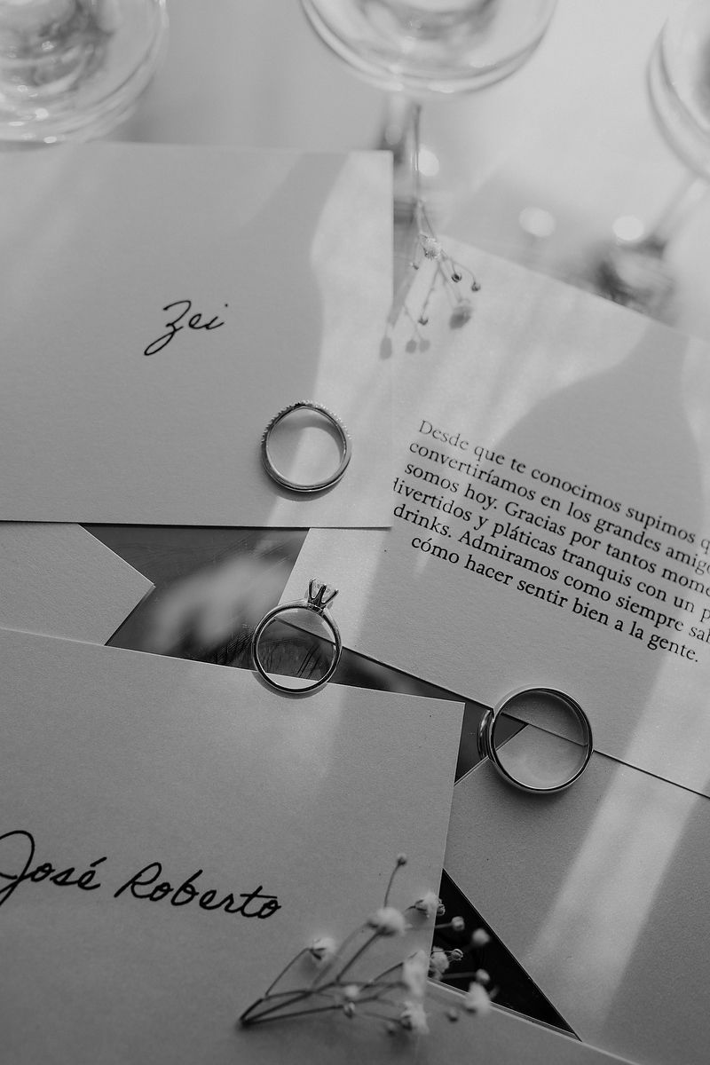Black and white close-up photograph of handwritten text on paper with wedding rings casting shadows.
