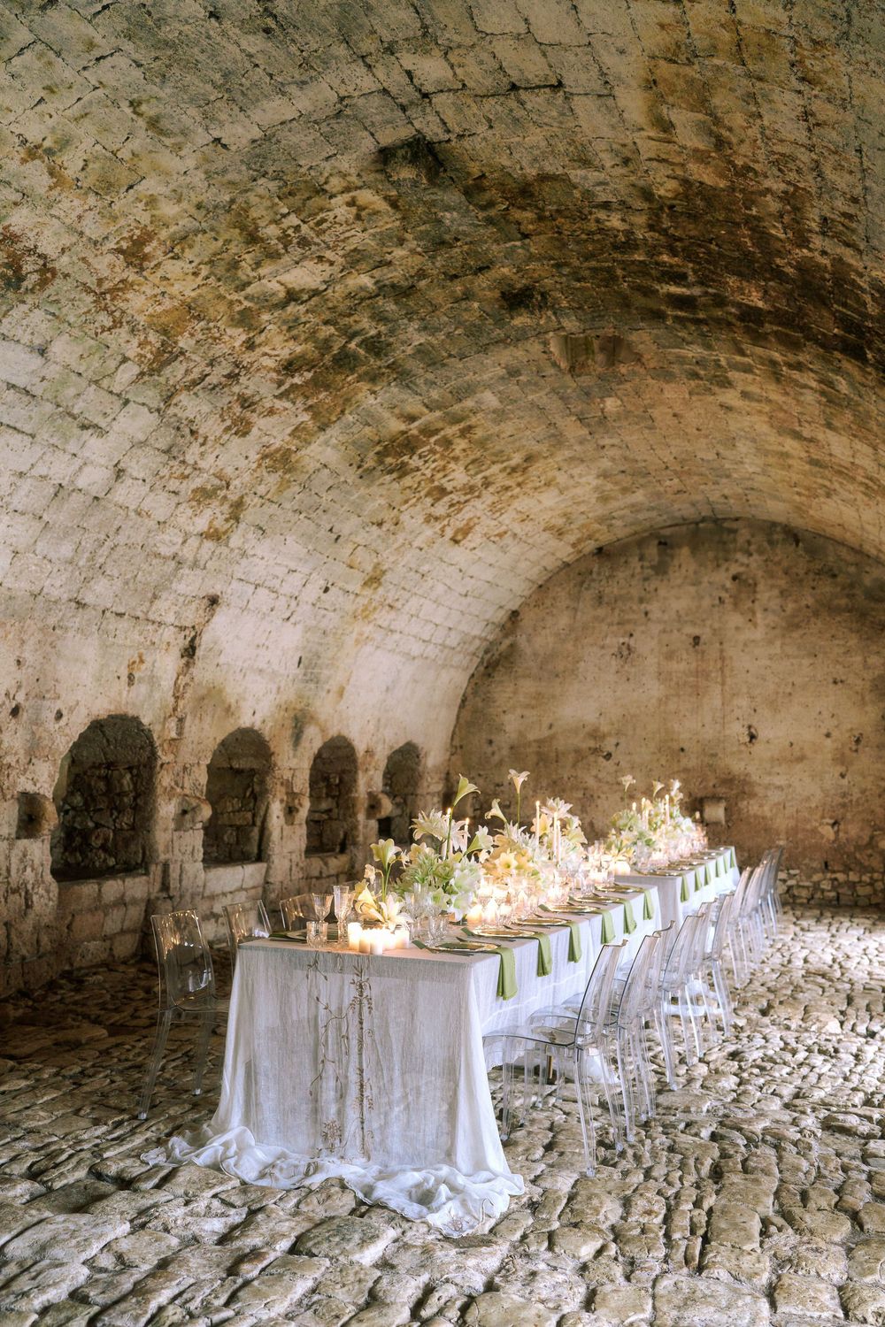 Long stone tunnel with arched ceilings and white tables set up for an elegant dining event. Puglia wedding photographer