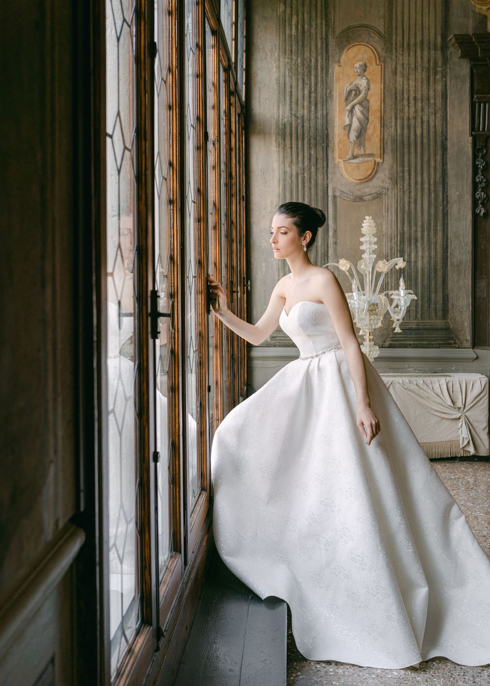 A bride in a voluminous white ballgown poses elegantly against classical columns in a historic mansion setting.