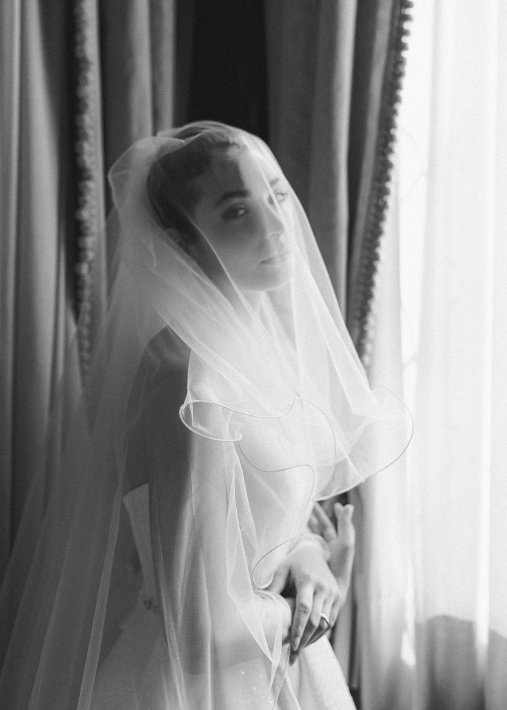 Artistic black and white portrait series showing bride in flowing veil against window light creating ethereal silhouettes.