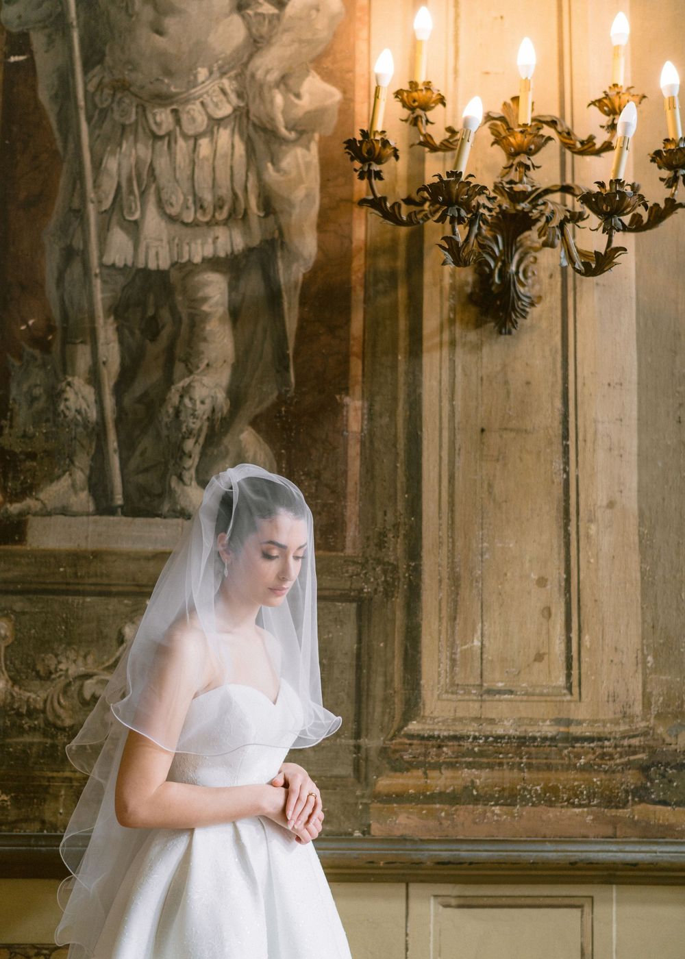 A bride in a flowing white dress and veil poses gracefully in a historic church interior with ornate candelabras.