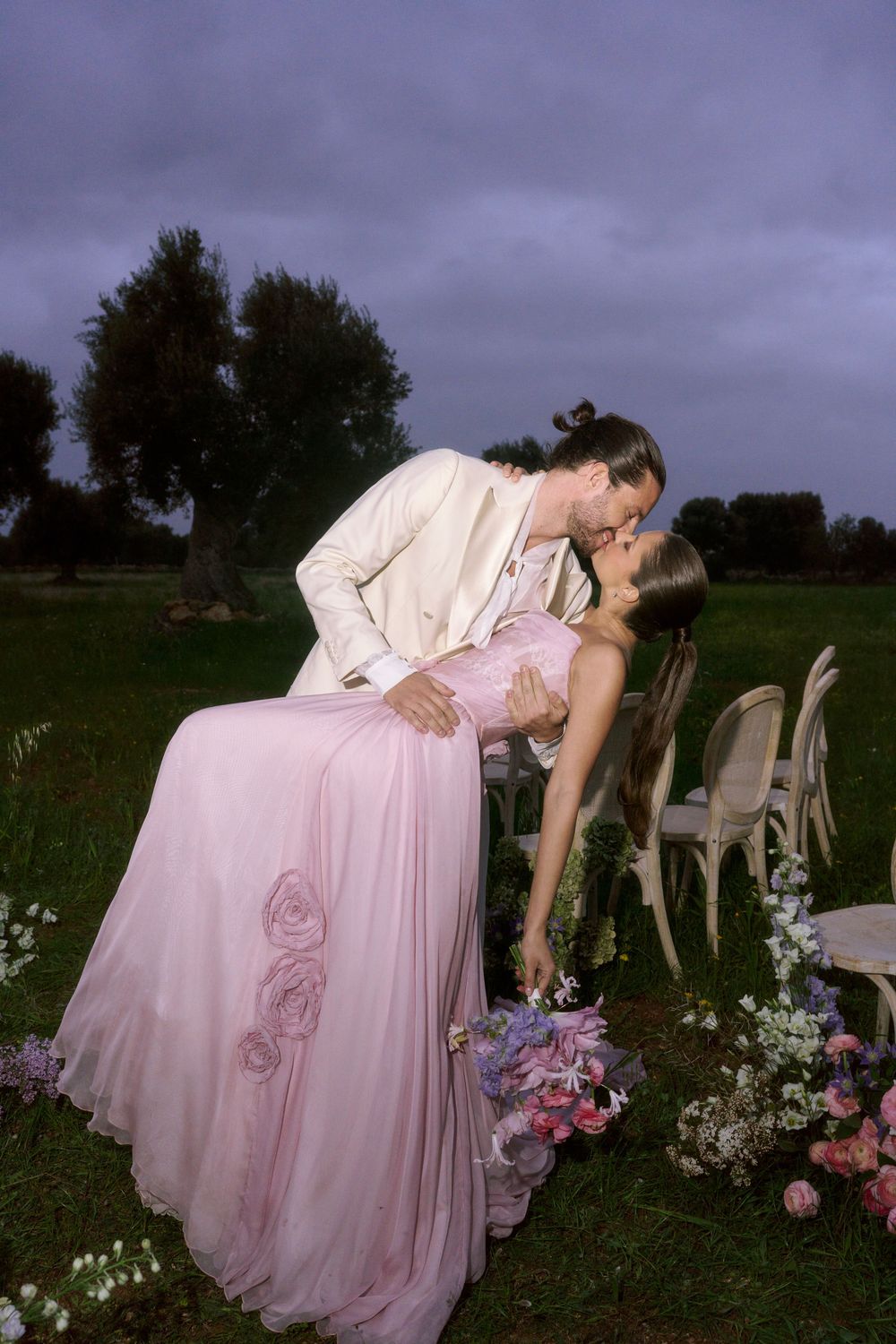 Romantic outdoor scene with pink flowy dress against moody sky and garden setting. Wedding photographer in Puglia