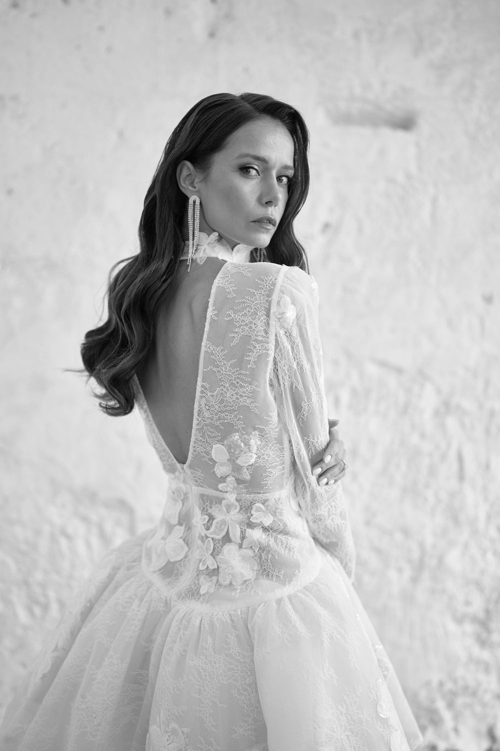 A woman in a romantic white lace wedding dress poses in a series of ethereal black and white portraits.