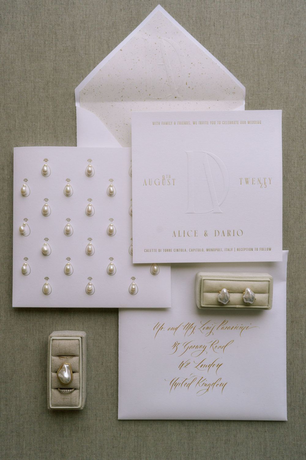 Elegant white wedding invitation suite with pearl details, gold calligraphy and matching ring boxes on gray linen background.