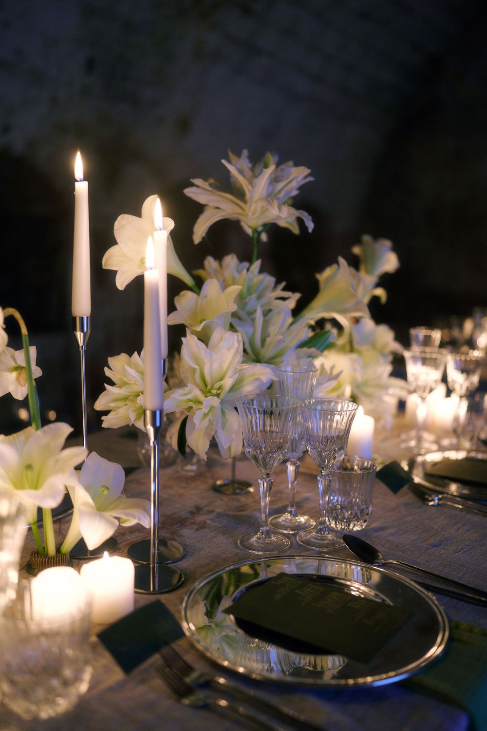 Elegant candlelit table setting with white lilies and crystal glassware creates a romantic dining atmosphere.