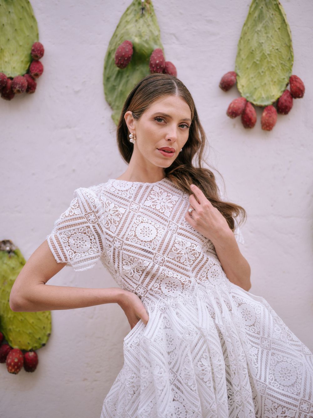 White lace dress with intricate geometric patterns displayed against a pink wall decorated with cactus leaves and berries.
