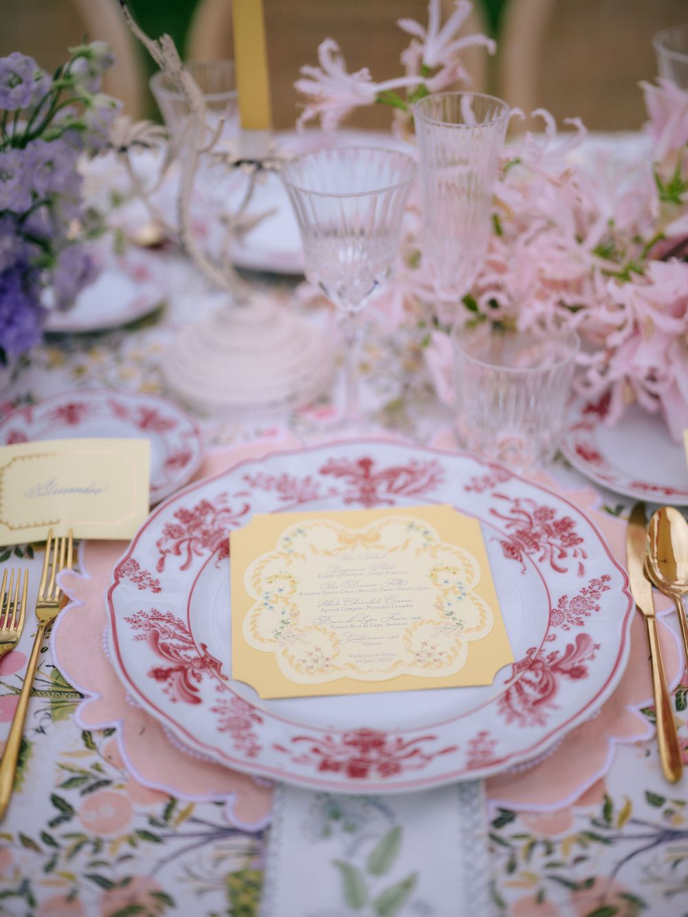 Elegant table setting with pink floral china plates, crystal glasses and delicate menu card in soft pastel colors.