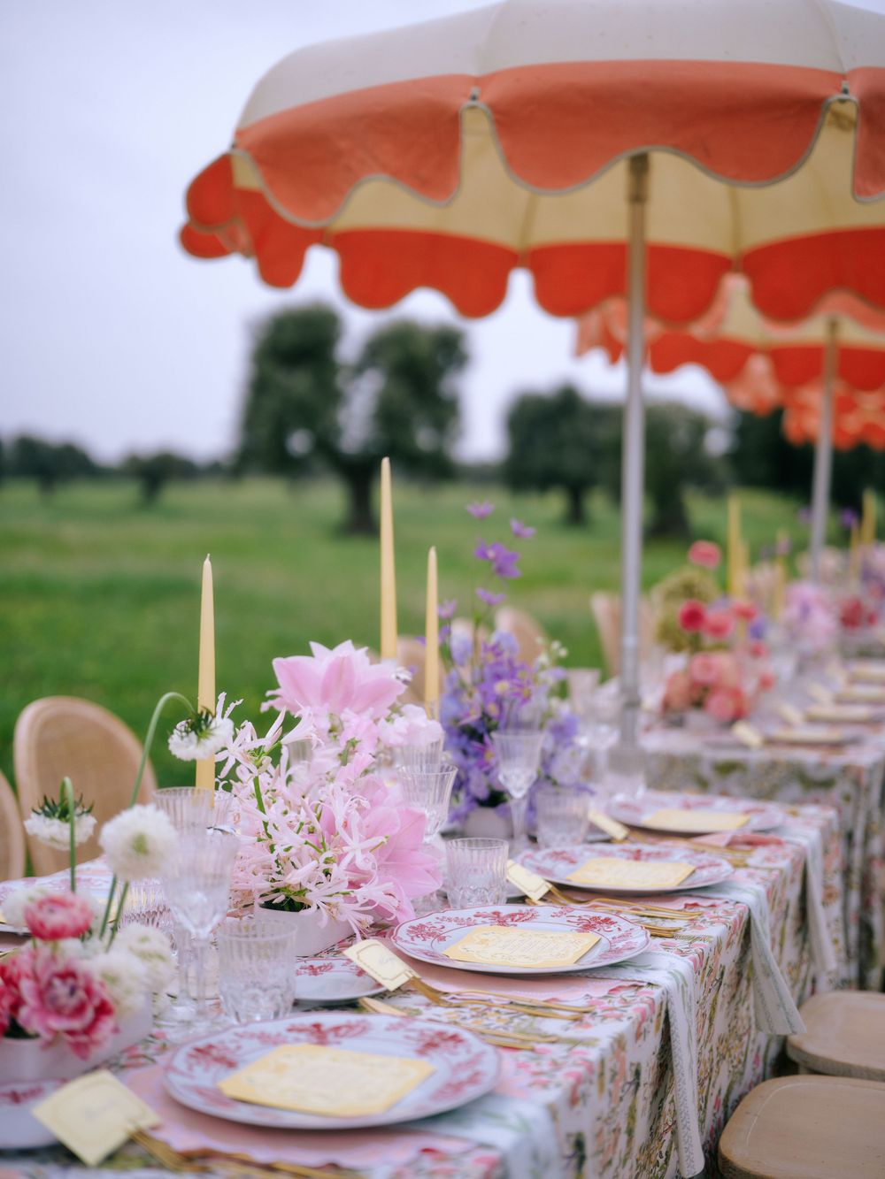 Elegant outdoor table setting with coral umbrellas, pink flowers, and delicate place settings for a garden party.