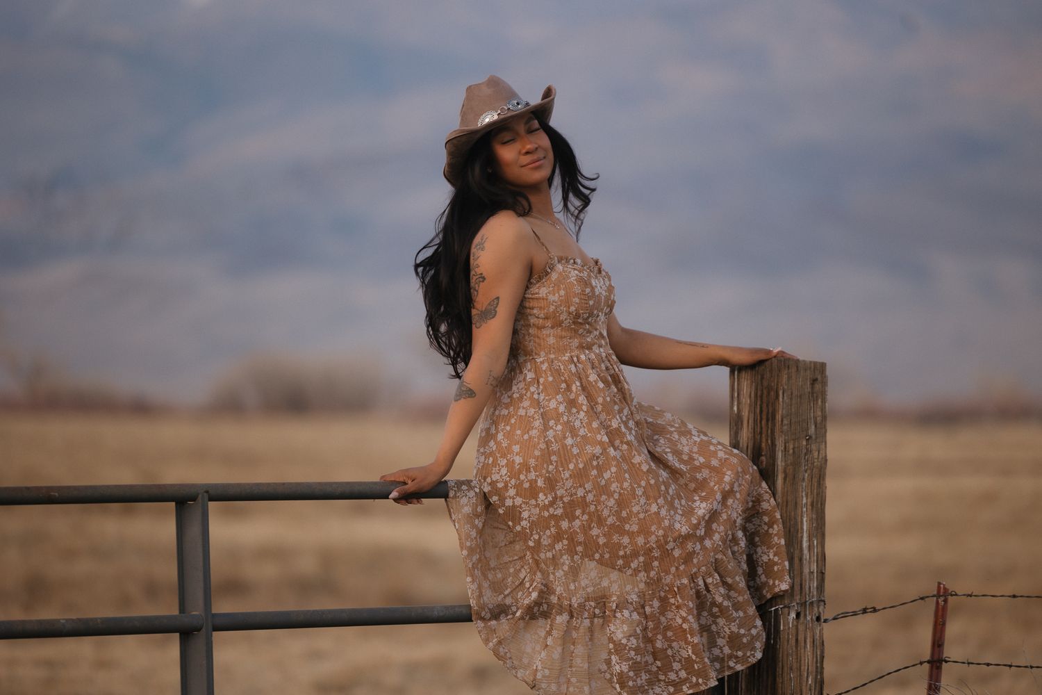 Woman in denim and sunglasses poses casually in natural outdoor setting.