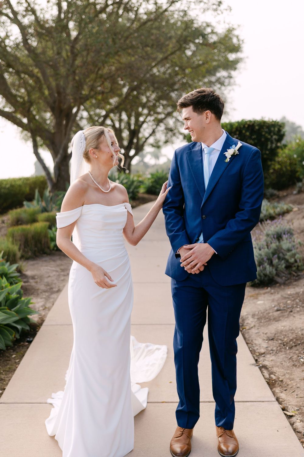 A couple share a candid moment in their wedding attire on a landscaped path.
