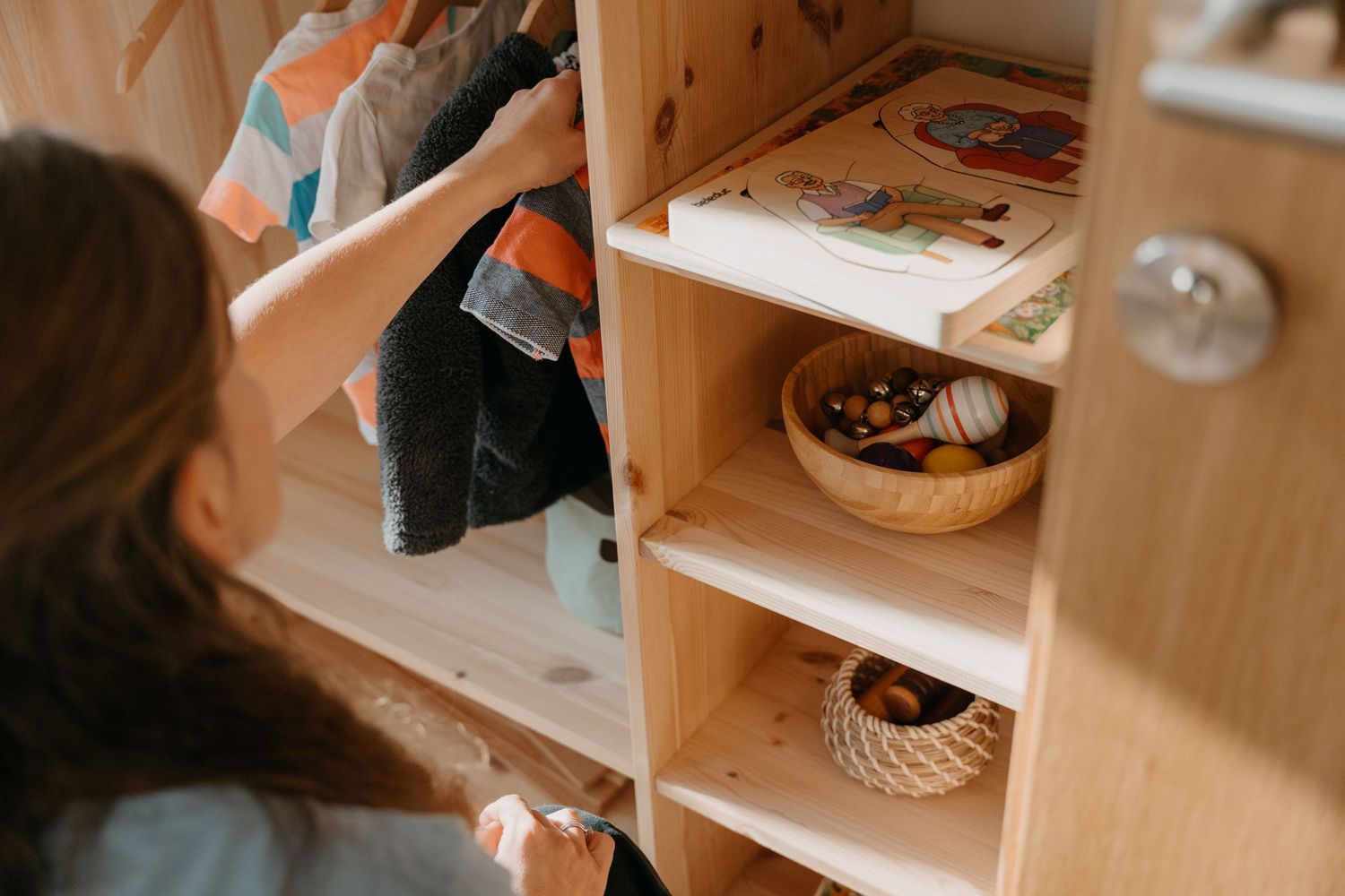 Child exploring educational materials on wooden Montessori shelves in a classroom setting.