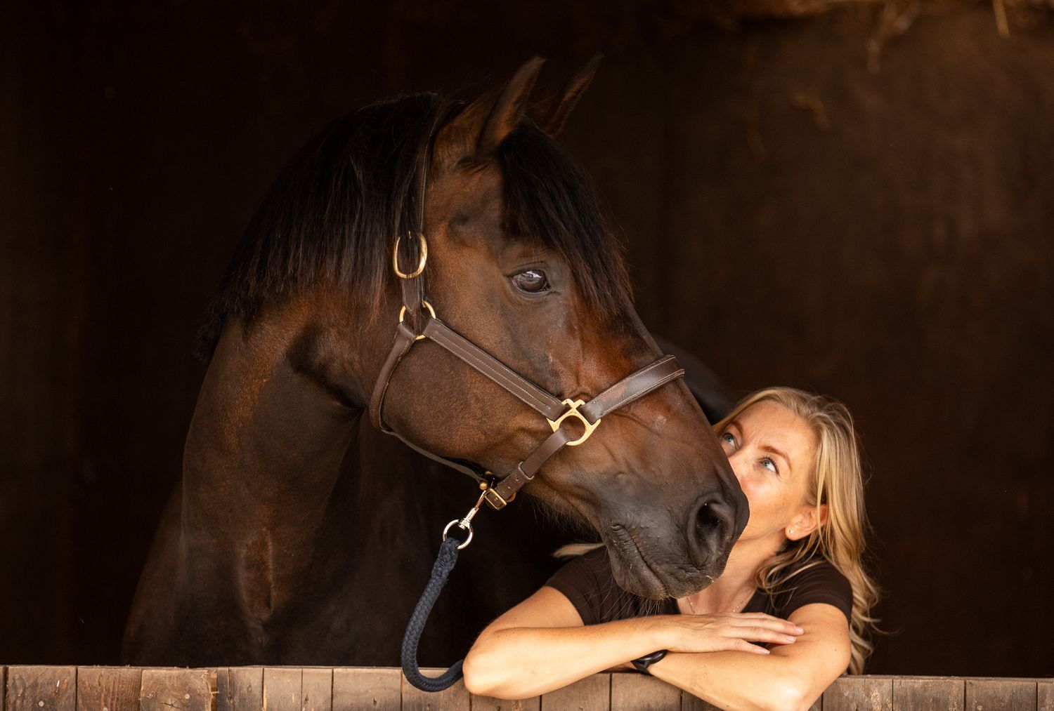 Two riders stand with their animals - a dog and a dark horse relaxing outdoors in a black and white photo.