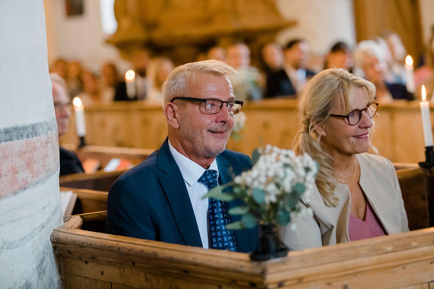 Wedding guests smile and laugh while seated in wooden church pews during a joyful ceremony.