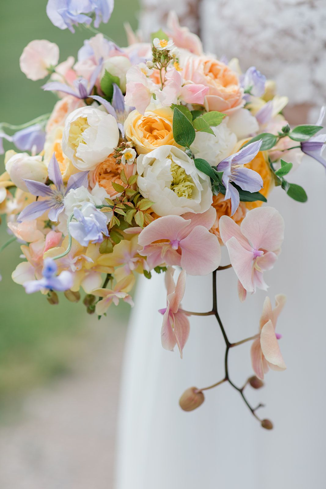 Delicate floral arrangement featuring soft pink and peach blooms with purple accents cascading from a white vase.