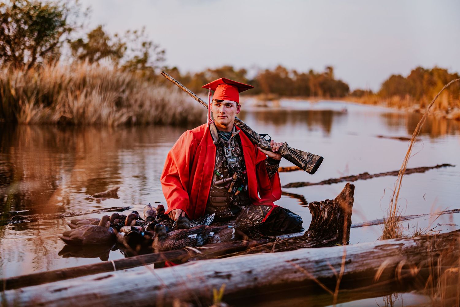 Duck hunter in red jacket positioned in wetland during golden sunset.